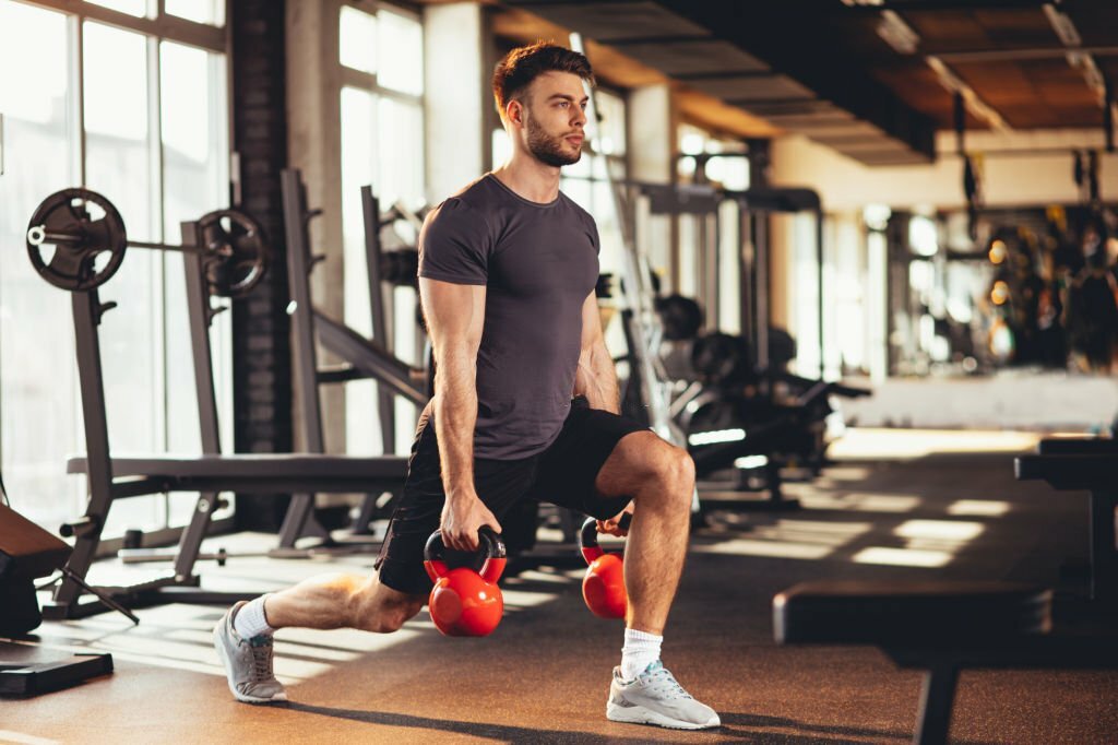 Handsome man legs workout with kettlebell in the gym
